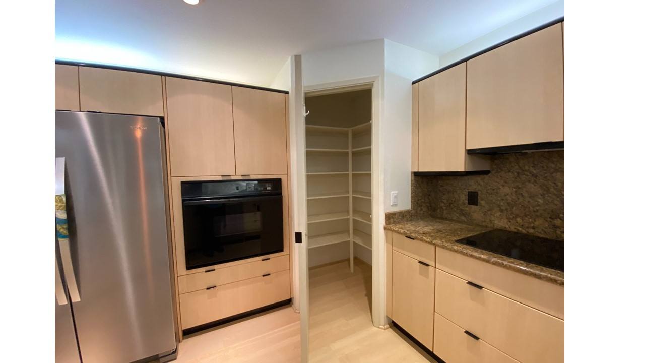 A kitchen with a stainless steel refrigerator and microwave, wooden cabinets, and a granite countertop.